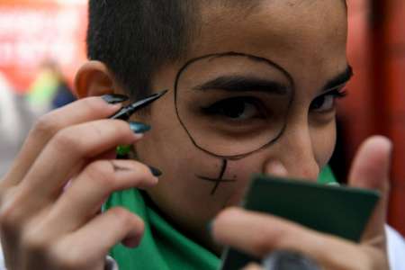 Una joven maquilla su rostro y porta el pañuelo verde.